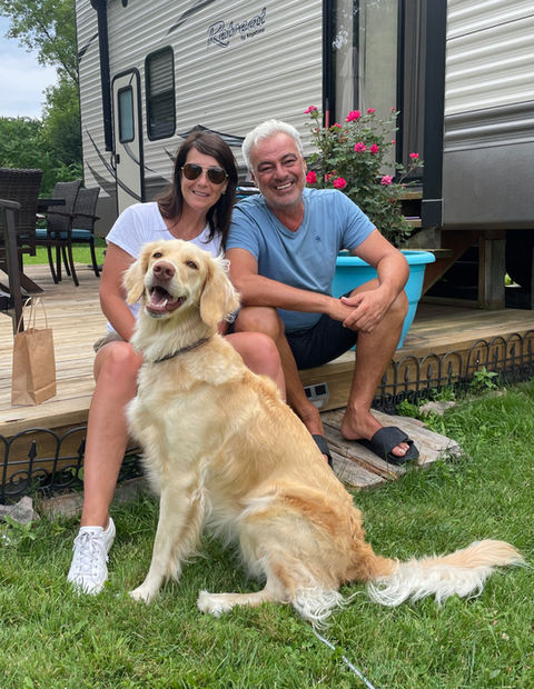 Smiling couple and golden retriever at a campsite deck