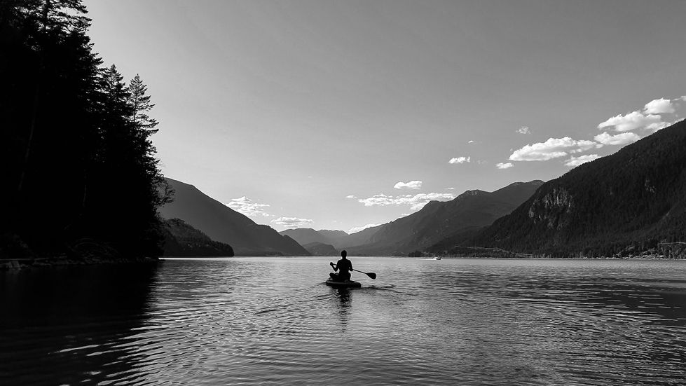 black and white photo of a paddleboarder on Lillooet Lake between mountains