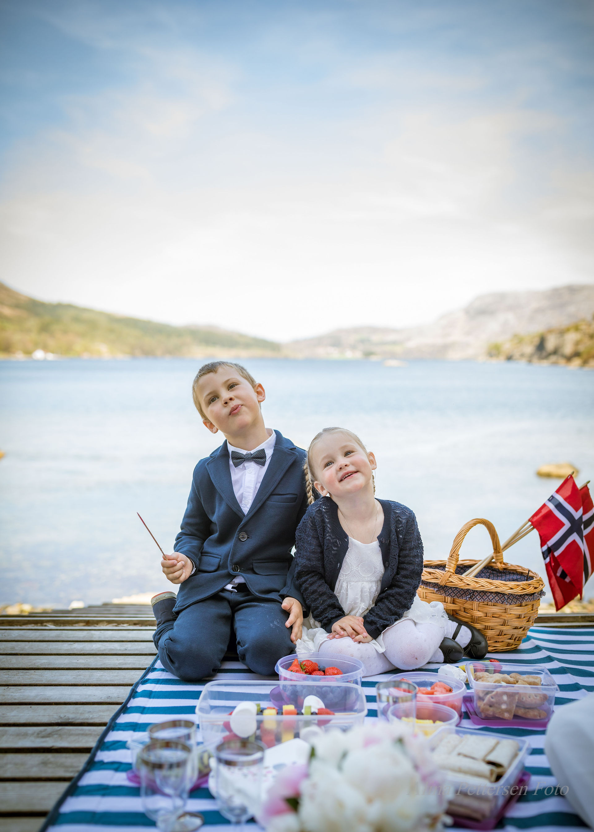 To festkledde barn ser opp ved vannet, med norsk flagg.