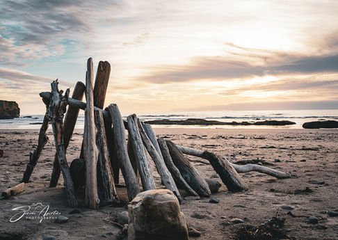 Fine art photography print of a peaceful Oregon coastal landscape with stacked driftwood at sunset with rich color and detail perfect for home or office decor.