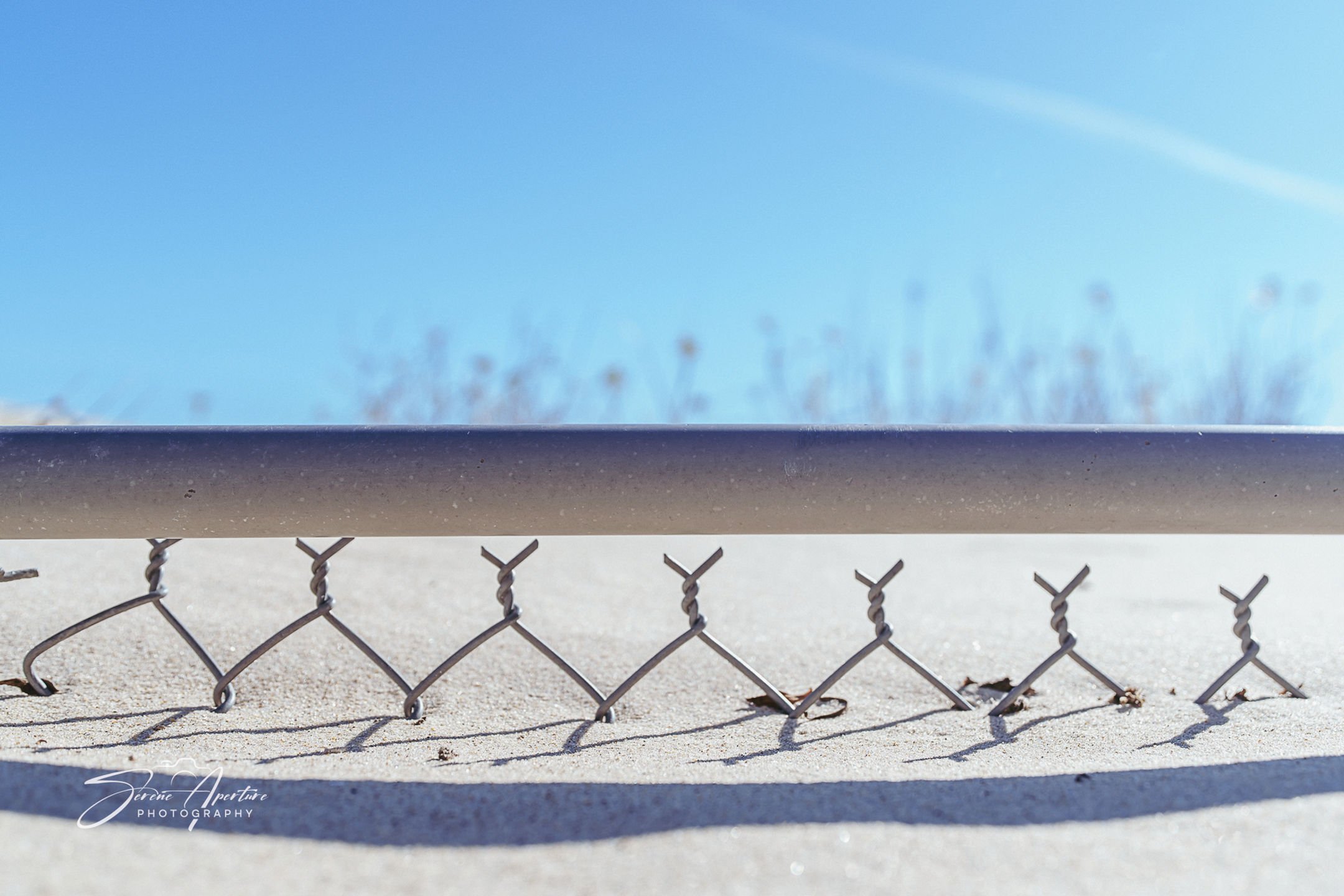 Top of chain link fence peaking out of a sand dune. Fine art perfect for home, office, lobbies, and more for all to enjoy!