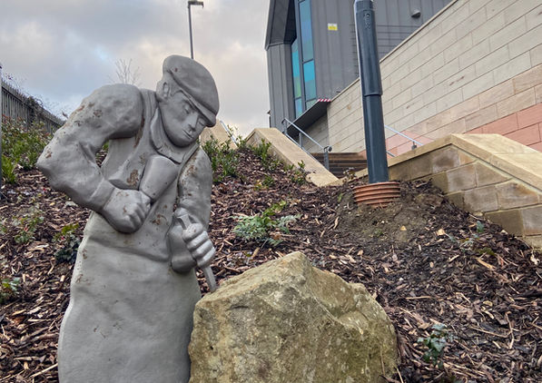 Statue of a stone worker beside a rock near modern buildings on the Loftus winter wellbeing walk.