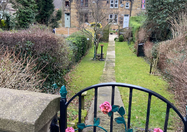 Stone cottage and garden path seen from a rose-decorated gate on the winter wellbeing walk.