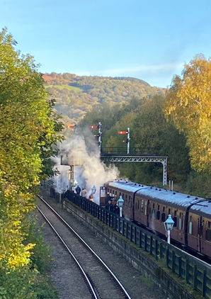 The Flying Scotsman waits at a Yorkshire platform surrounded by autumn trees and semaphore signals.
