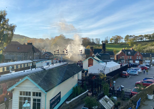 Crowds gather at a Yorkshire station as the Flying Scotsman arrives in steam under a bright blue sky.