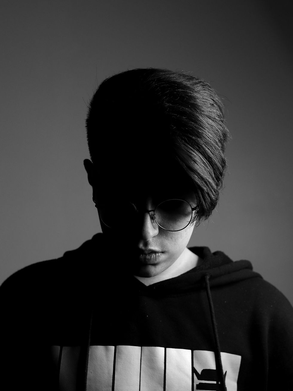 Black and white image of a boy with glasses looking down. His hair is covering a lot of his face.