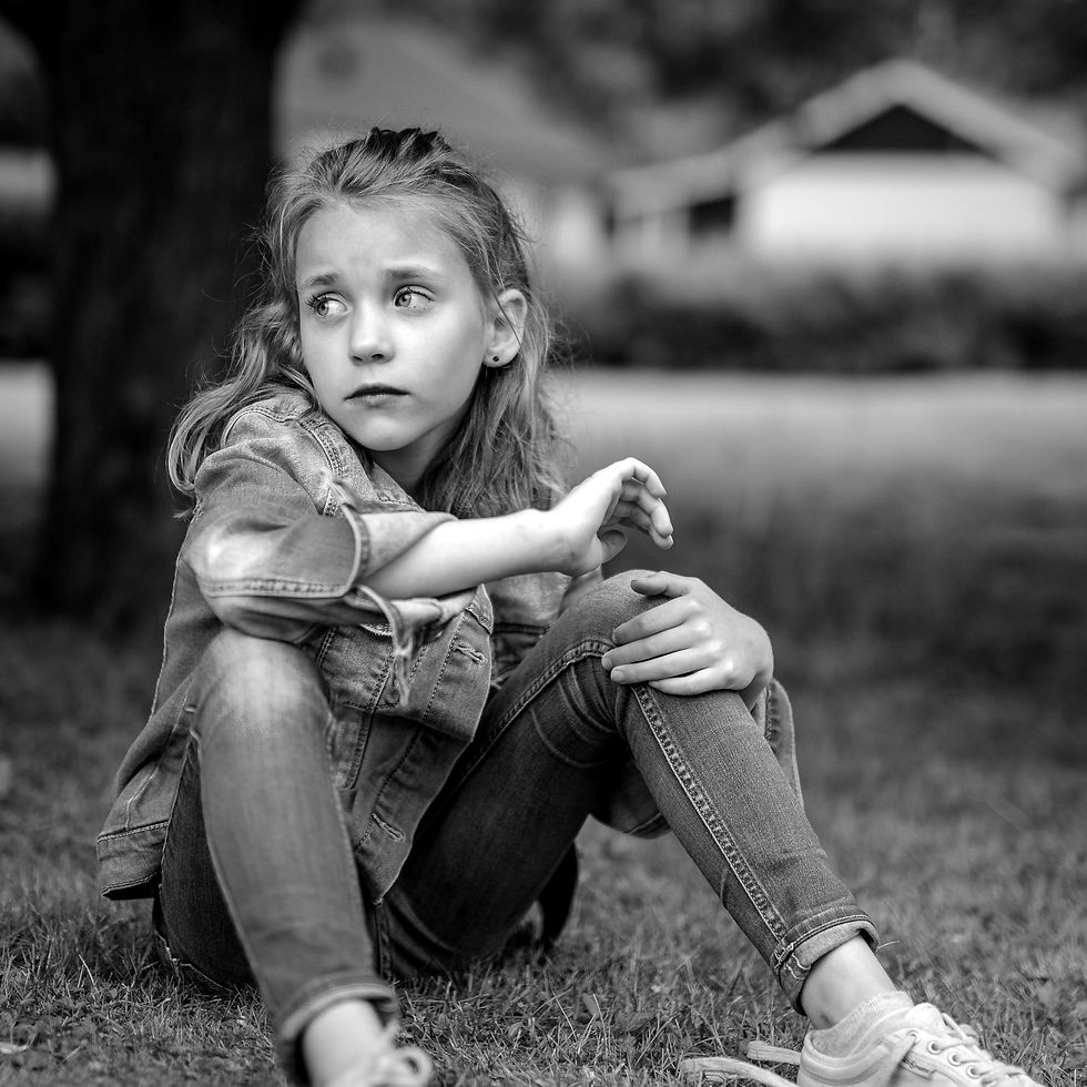 Black and white portrait picture of a girl sat on the grass looking away to her right.