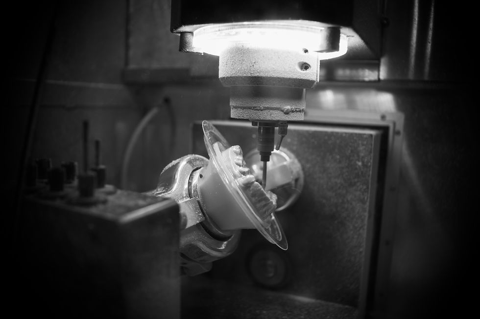 Dental milling machine carving a tooth model in a dark workshop, with bright overhead light and grayscale industrial feel