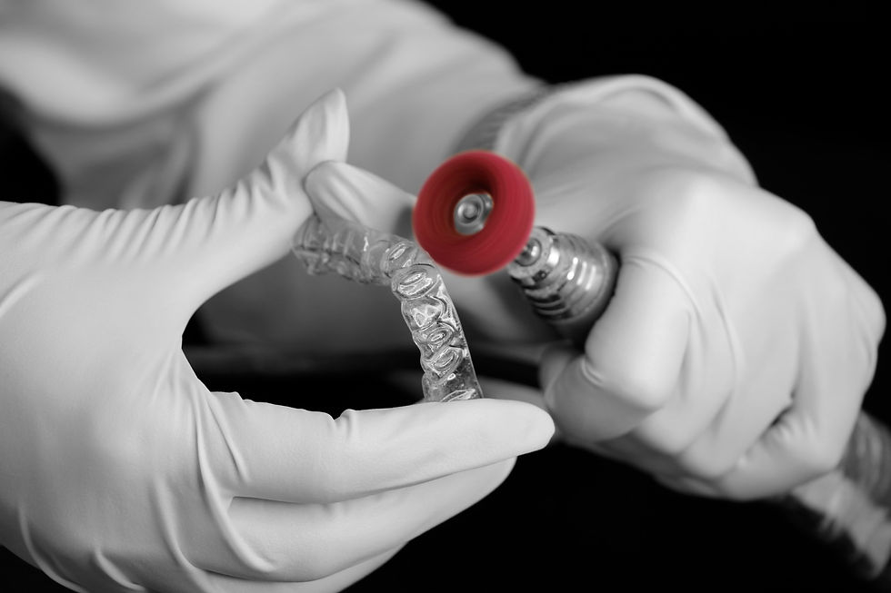 Gloved hands polish a clear dental aligner with a red rotary tool on a black background, close-up and clinical.