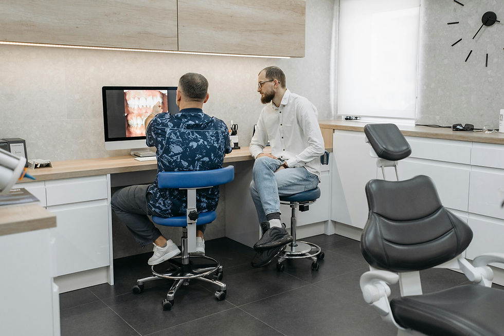 Two men in an office, seated at a desk with a computer showing dental images. Modern interior with white cabinets and a clock on the wall.