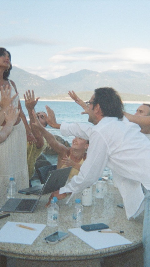 Groupe de personnes félicitant une femme, montagnes et mer en arrière-plan.