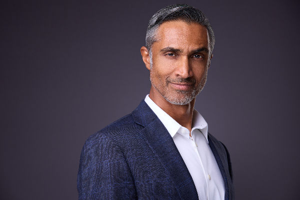 A headshot of a middle aged business executive with salt and pepper hair and wearing white shirt and blue suit jacket