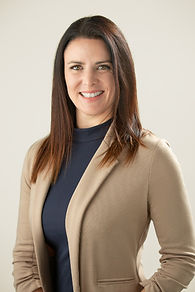 A corporate headshot of a business woman wearing a tan jacket and navy blue shirt