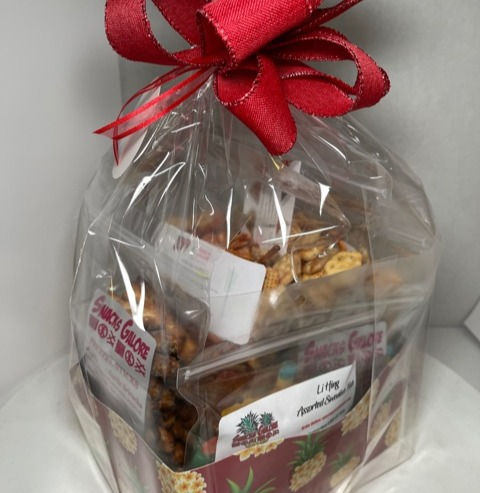 Gift basket wrapped in clear plastic and topped with a red bow, containing assorted snacks. Background is plain white. Bright and festive.