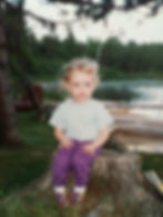 me at age 3 sitting on a tree stump by a lake, canoes and a dock behind me in the early 90's in an outfit i wish i still had (purple pants, white tee, white socks, multi-colored itty bitty bowling Keds). kids are cute, this is a cute picture. film photo taken by my mama Kris Monson.