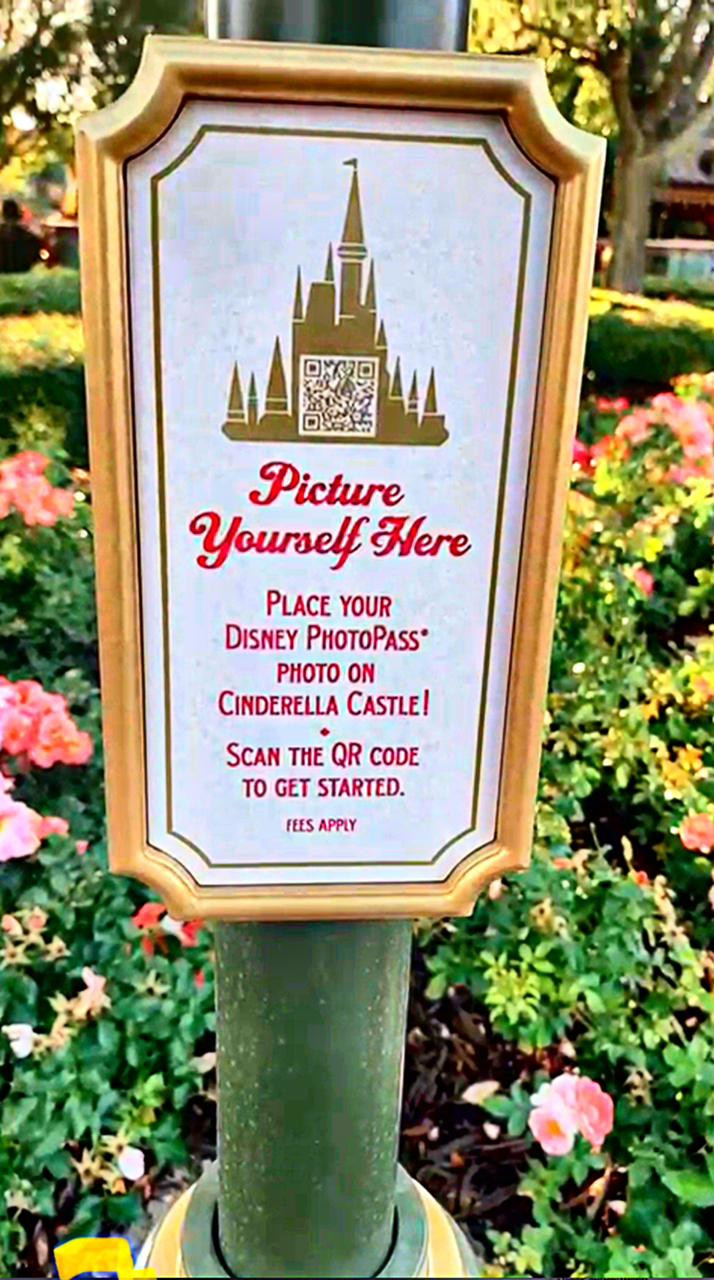 Placa no jardim perto do castelo com QR code para acessar o recurso Mural of Memories no My Disney Experience.