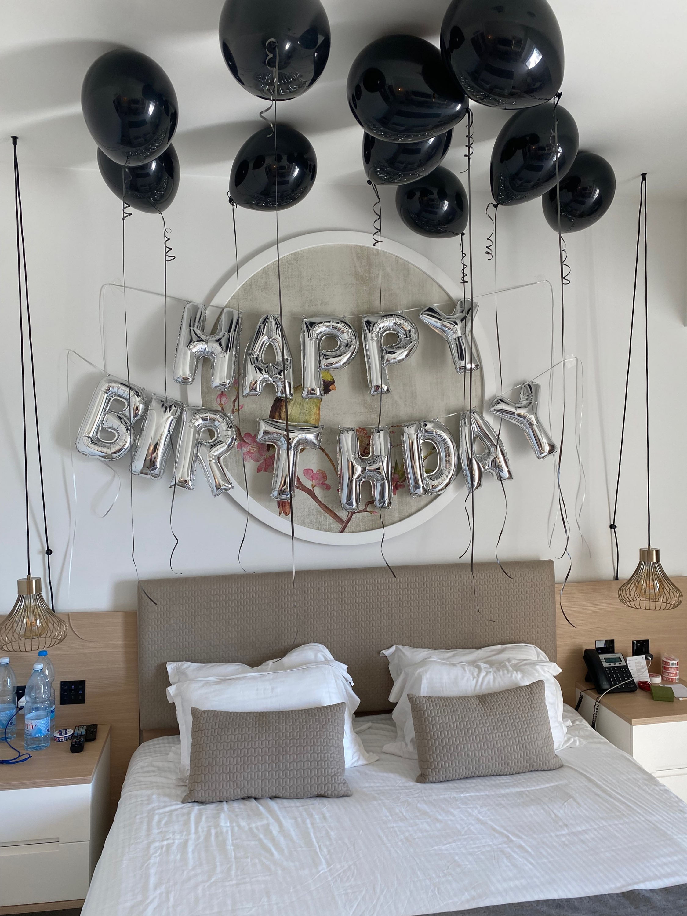 Happy Birthday silver balloons with black balloons, a bed, and decorations.