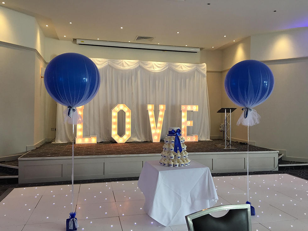 Two blue balloons with LOVE illuminated sign at party event background.