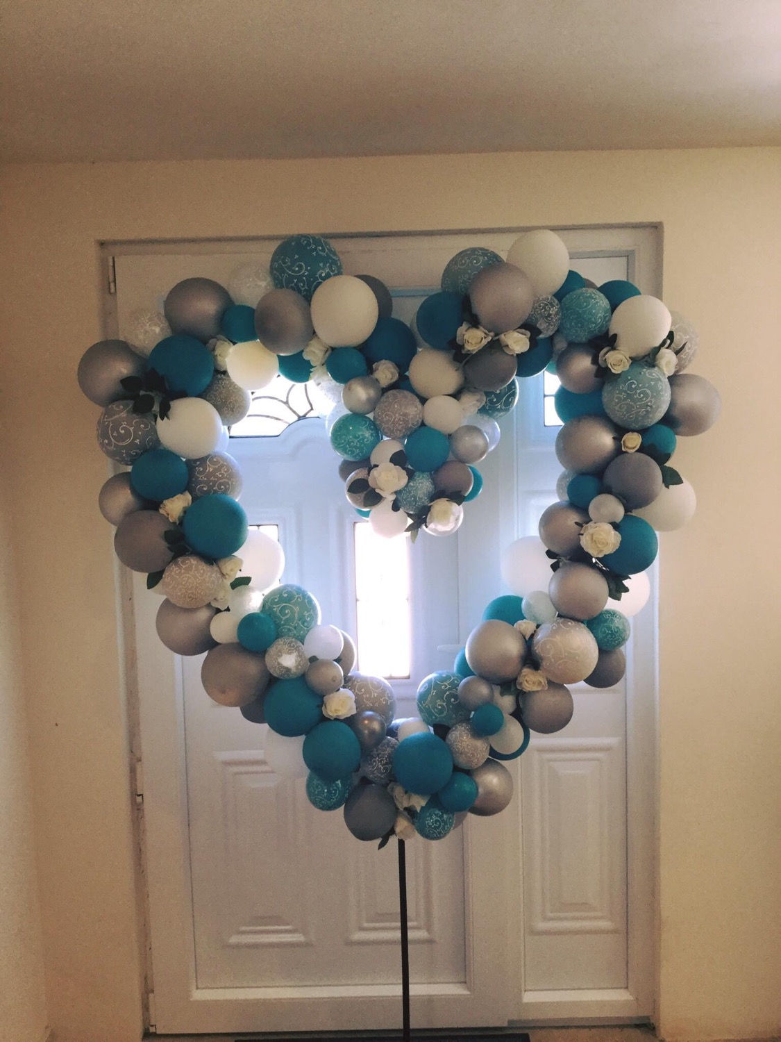 Heart-shaped balloon display with white door and mixed blue, silver, and white balloons