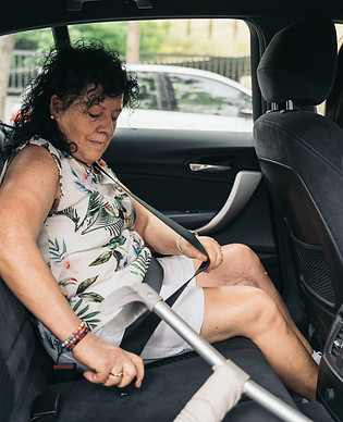 Senior woman with crutches fastening her seatbelt while sitting in the backseat of a car,