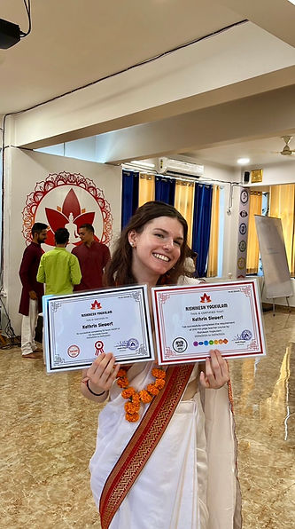 Hier ist Kathi in einem Sari zu sehen und hält ihre beiden Yoga Zertifikate hoch.