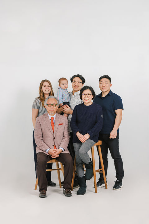 Multigenerational family studio portrait celebrating a baby’s first birthday – adults seated and standing together in a clean white background.
아기의 첫돌을 기념하기 위해 모인 대가족의 스튜디오 사진 – 흰 배경 앞에서 어른들이 나란히 앉고 서 있는 구성