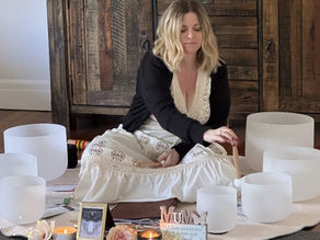 a lady sitting on a round mat playing crystal sound bowls