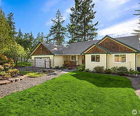 A yellow house with a bright green lawn nestled in a wooded location.