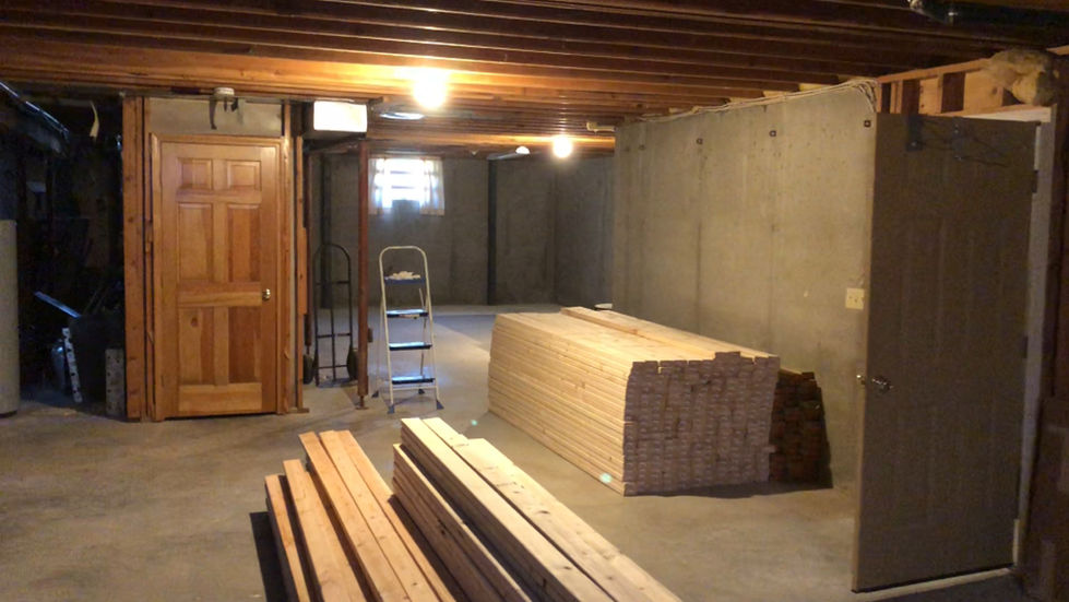 Unfinished basement framing project by Brian’s Drywall Services (BDS) in Overland Park, KS showing stacked 2x4 lumber, exposed ceiling joists, and concrete walls ready for drywall and painting services throughout the Kansas City metro area