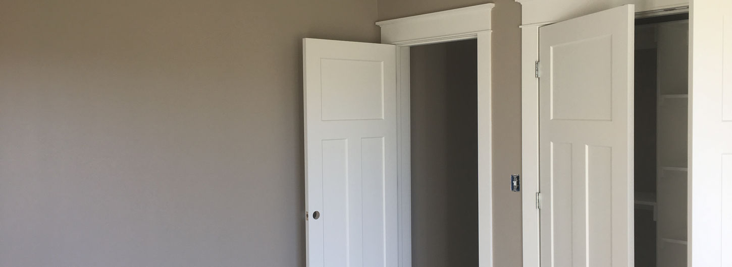 Completed bedroom remodeling project showcasing professional interior painting with smooth tan walls, a pristine flat white ceiling, crisp white painted doors, and matching craftsman-style trim casings around the closet and hallway entryways, expertly finished by (BDS) Brian's Drywall Services in Kansas City, MO.