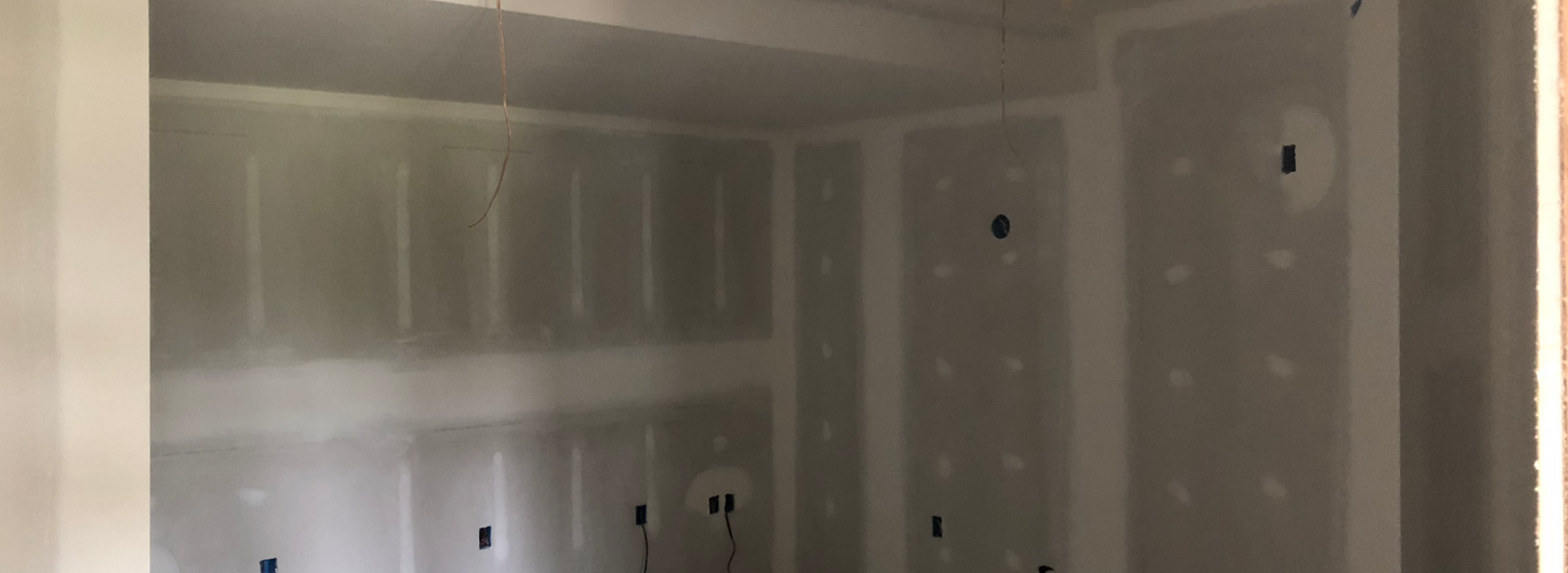 Residential remodeling project in progress showing professional drywall finishing with taped and mudded seams, skim-coated joints, and smooth drywall patching ready for interior painting in an unfinished home basement or addition with exposed wiring and concrete floors, by (BDS) Brian's Drywall Services in Raymore, MO.