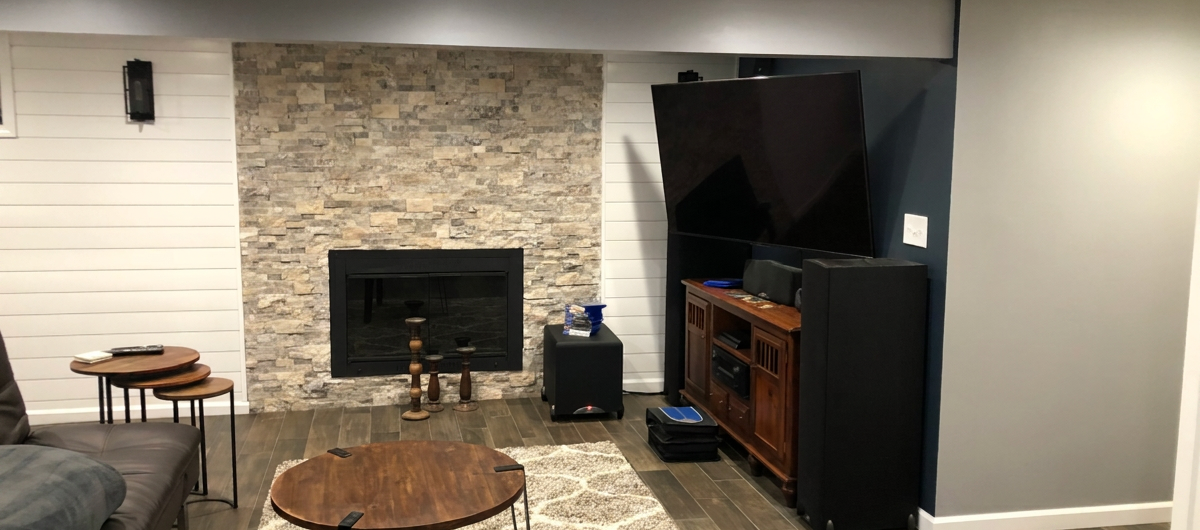 Finished beautiful painted basement remodel in Blue Springs, MO by Brian's Drywall Services (BDS). Stunning completed basement featuring stone fireplace, white shiplap accent wall, large wall-mounted TV, wood media console, round coffee table on area rug, and modern luxury finishes after full residential renovation