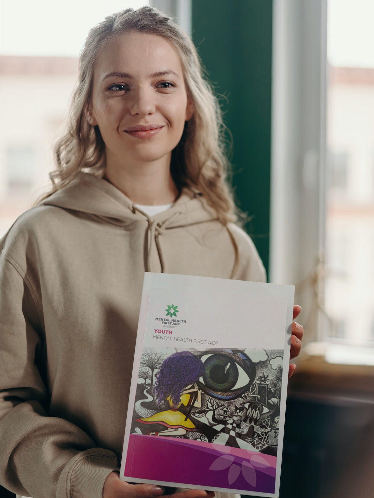 A young lady holding a book, titled Youth Mental Health First Aid