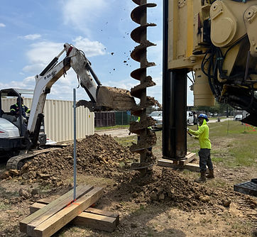 Drilling rig with a large auger beside an excavator and crew at a foundation site