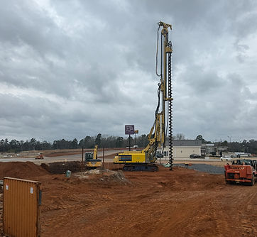 Auger cast piling rig on a cleared construction site beneath cloudy skies