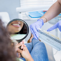 A woman holding a mirror looking at her white teeth after a teeth whitening operation