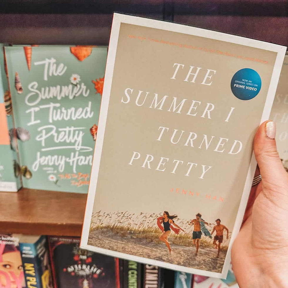 Hand holding "The Summer I Turned Pretty" book by Jenny Han. Background shows similar books on a shelf. Light, summery cover design.