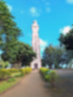 Point Venus Lighthouse, built in 1867. A tall lighthouse stands amid trees and shrubs under a bright blue sky. The mood is peaceful.