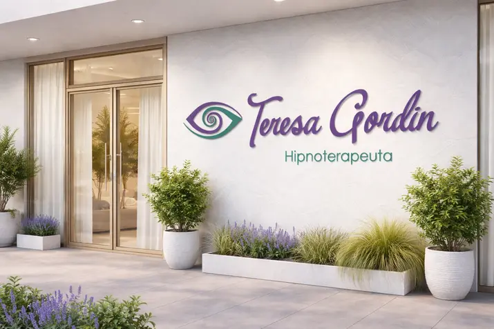 Fachada da clínica de atendimento em iluminação natural do dia. Na parede branca com textura suave, destaca-se o logotipo em relevo com o símbolo do olho e o nome 'Teresa Gordin' em tom lilás e 'Hipnoterapeuta' em verde-esmeralda. À esquerda, avista-se a porta de entrada em vidro com caixilharia em alumínio champanhe e cortinas brancas ao fundo. Na base da parede e em vasos de cerâmica clara, compõem a cena plantas verdes e pequenas flores em tom lavanda.