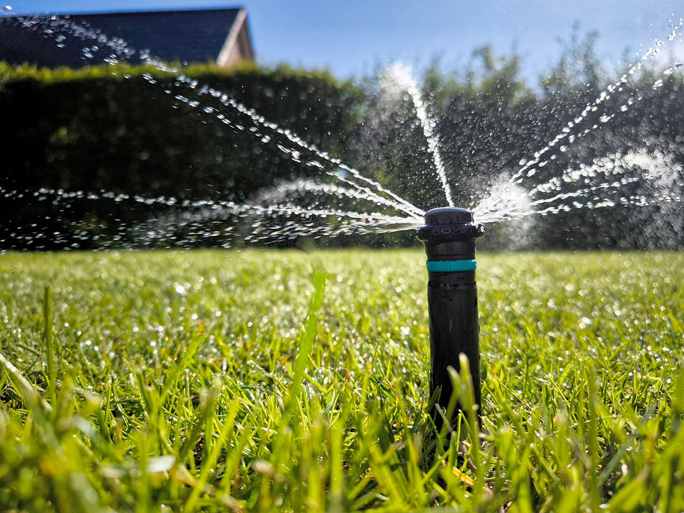 An irrigation sprinkler watering a beautiful, green lawn under a clear sky, creating a nat