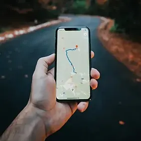 A person's hand holding a phone opened up to Google Maps, o road is in the background