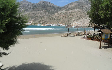 The golden sparkled beach of Platis Gialos on the Island of Sifnos. The valleys and mountains in the background. Umbrellas and sunbeds cover the endless beach.