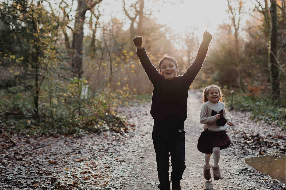 Two children running through Leigh Woods, the boy wearing black and the little girl in a white jumper