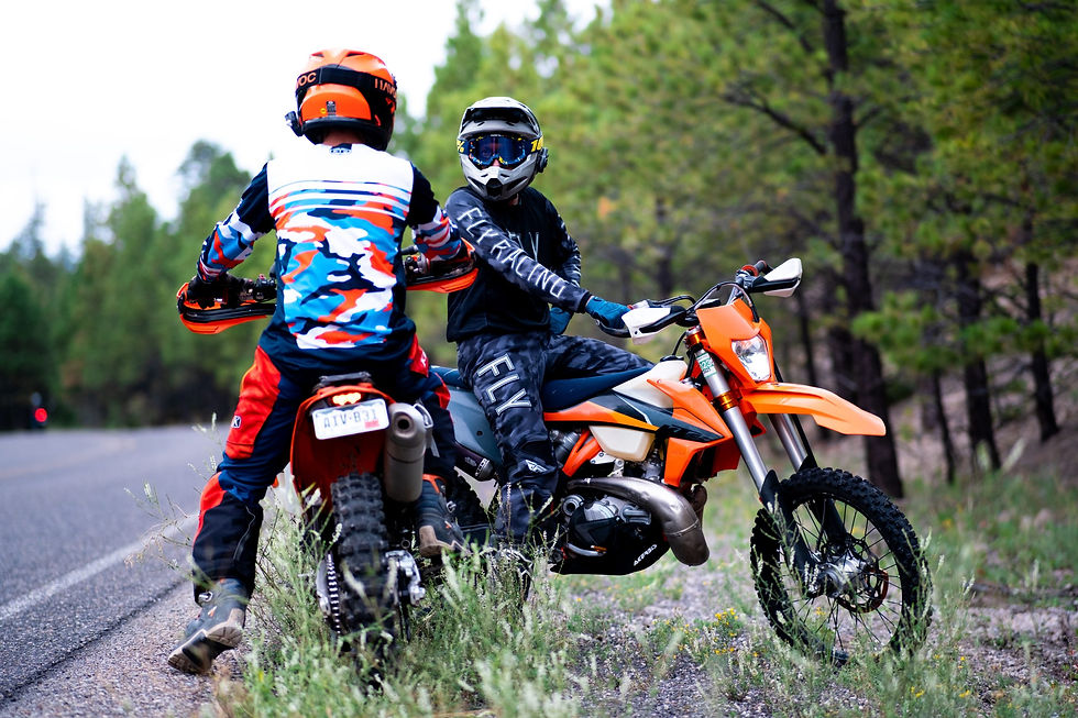 Two men on dirt bikes sitting next to each other by a road.