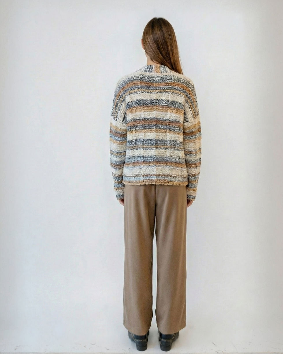 Woman wearing striped sweater and brown pants stands against a white background.