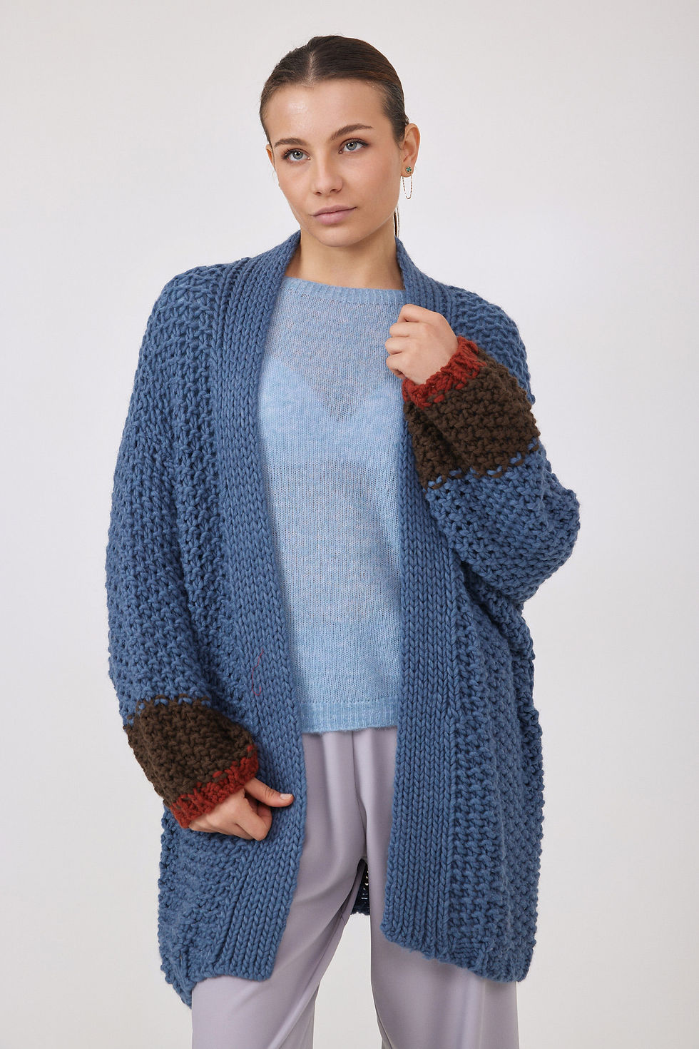 Woman wearing blue cardigan with brown and red sleeves, neutral background