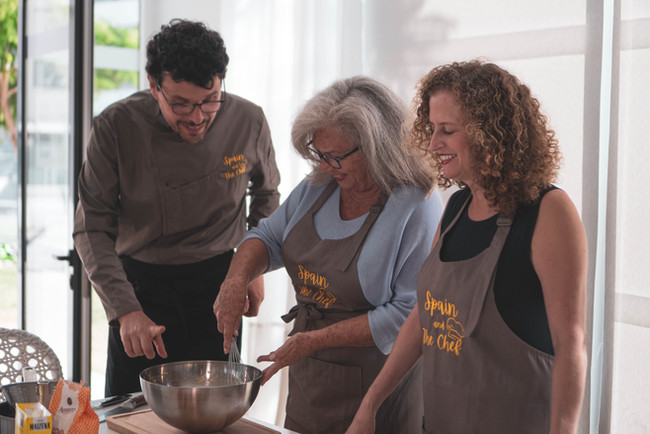 Two middle aged ladies in a cookery class with a private chef preparing a dish and having fun.,