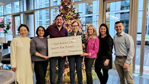 Seven people smiling at the camera. Four people in the middle are holding a check.