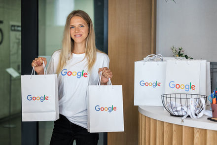 Hosteska drží dárky Google v papírové tašce.
