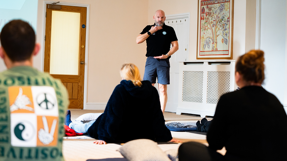 A man standing in front of three people in a well lit room, teaching about lung capacity.